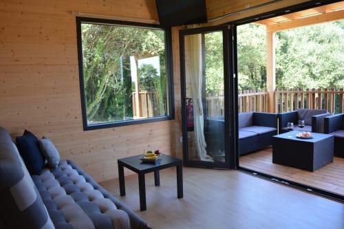 Interior moderno de cabaña con paredes de madera, asientos azules y puertas de cristal que abren a la terraza de montaña en Cabañas Compostela