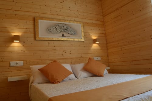 Acogedora habitación de cabaña de madera en Cabañas Compostela con cama queen, almohadas naranjas y cuadro de árbol sobre el cabecero