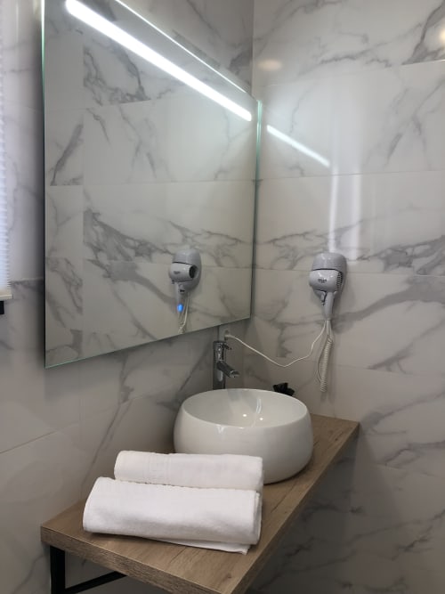 Baño moderno en Cabañas Compostela con azulejos de mármol, espejo LED, lavamanos de cerámica blanca y toallas blancas sobre mostrador de madera