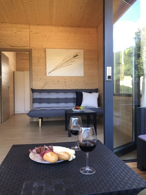 Interior moderno de cabaña de madera con sofá a rayas, mesa negra, copas de vino y vista a la montaña en Cabañas Compostela