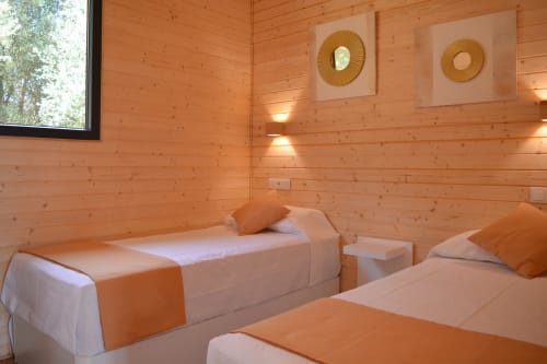 Acogedora habitación de cabaña de madera en Cabañas Compostela con camas gemelas, detalles naranjas y ventana con vista al jardín en Santiago de