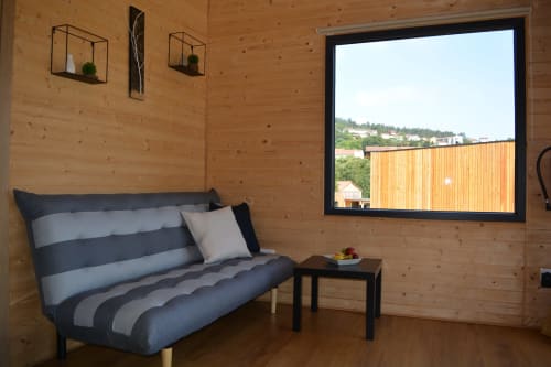 Interior acogedor de cabaña de madera en Cabañas Compostela con sofá a rayas, televisor de pantalla plana y vistas al jardín desde amplias ventanas