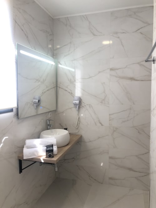 Baño moderno con lavabo redondo blanco, espejo, zona de ducha y vanidor de madera en Cabañas Compostela, Santiago de