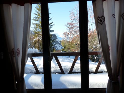 Vue enneigée du balcon des Chalets Cocody à Jausiers avec montagnes et sapins visibles à travers les portes-fenêtres