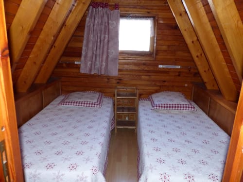 Chambre douillette de chalet en bois avec deux lits jumeaux, rideaux à carreaux rouges et poutres apparentes aux Chalets Cocody, Jausiers