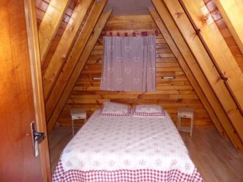 Chambre douillette sous les toits aux Chalets Cocody à Jausiers avec poutres en bois, literie vichy rouge et charme authentique de chalet montagnard