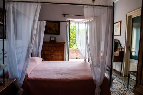 Elegante letto a baldacchino con biancheria rosa presso il B&B Valle Allegra di Gravina di Catania, vista del giardino attraverso le porte francesi