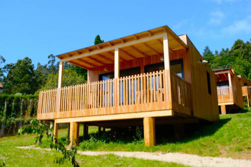Cabaña de madera con terraza y porche cubierto rodeada de paisaje verde en Cabañas Compostela