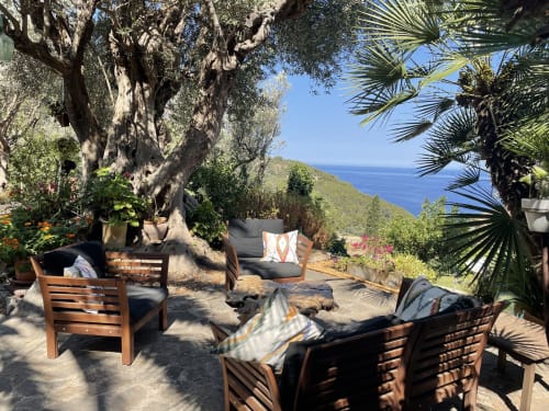 Terraza costera del Petit Hotel Sa Plana en Estellencs con sillas de madera, vistas al mar y jardines mediterráneos bajo árboles antiguos