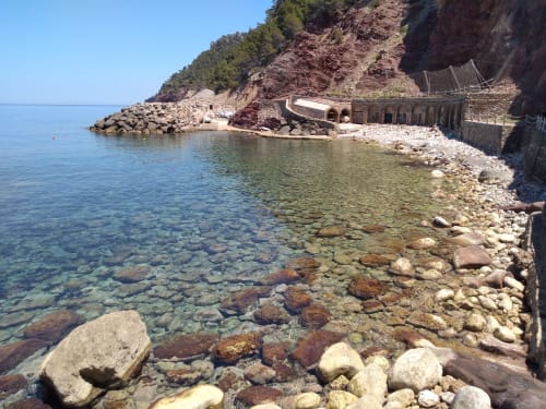 La cala cristalina del Petit Hotel Sa Plana con costa rocosa, muro de piedra protector y espectacular telón de acantilados