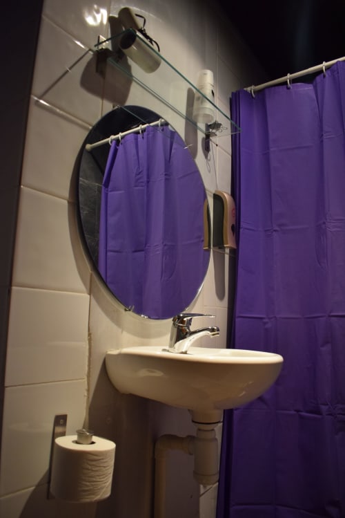 Baño moderno del hostel La Calma De Bellver con espejo redondo, lavamanos blanco y cortina de ducha morada