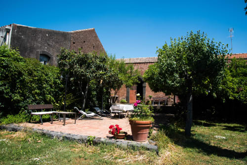 Cortile rustico del B&B Valle Allegra a Gravina di Catania con vasi in terracotta, fiori rossi e edifici in pietra