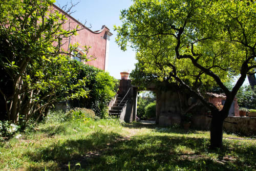Cortile rustico del B&B Valle Allegra con edifici rossi vintage, vegetazione rigogliosa e strutture in pietra a Gravina di Catania