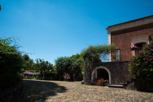 Villa in pietra B&B Valle Allegra con fiori rosa, ingresso ad arco e balcone a Gravina di Catania