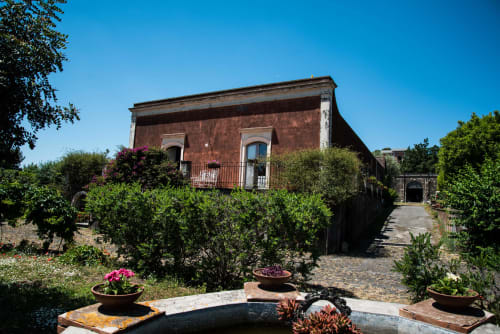 Corte della B&B Valle Allegra a Gravina di Catania con villa in terracotta, piante fiorite e sentiero in pietra sotto cielo azzurro