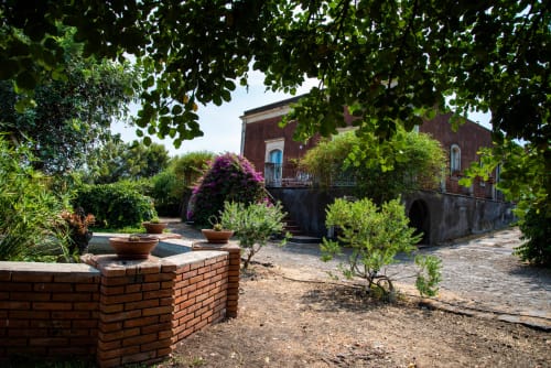 Cortile del giardino di B&B Valle Allegra a Gravina di Catania con muri in laterizio, buganvillee fiorite e ulivi