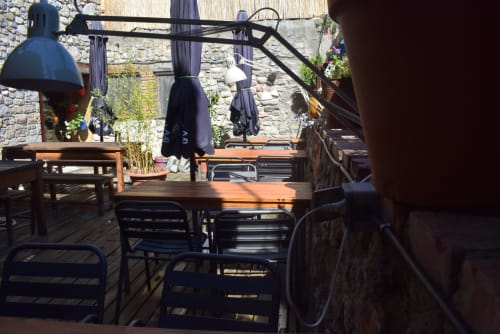 Terraza exterior del hostal La Calma De Bellver en Bellver de la Cerdanya con mesas de madera, sillas negras y muros de piedra.