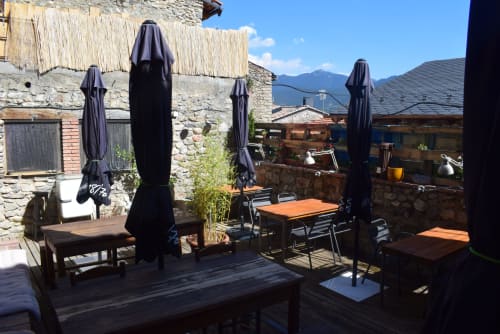 Terraza exterior del albergue La Calma De Bellver con sombrillas negras, mesas de madera y vistas a la montaña