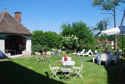 Jardin spacieux d'Aux Fleurs de Cerises B&B au Plessis-Luzarches avec tables de repas, transats et parasol