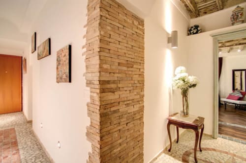 Elegante corridoio nell'appartamento Tommaso di Orso Luxury Apartments a Roma, con colonna in mattoni a vista e arredamento classico