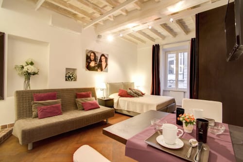 Bernini apartment at Orso Luxury Apartments in Rome features beige sofa, bed with pink accents, exposed beams, and dining