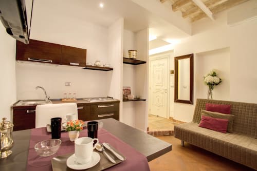 Bernini apartment at Orso Luxury in Rome features dark wood kitchen, dining area with purple table, and green sofa with city