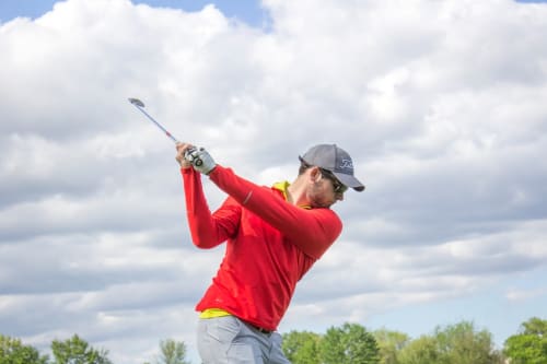 Golfeur en chemise rouge en plein swing au golf Le Plessis Luzarches près d'Aux Fleurs de Cerises