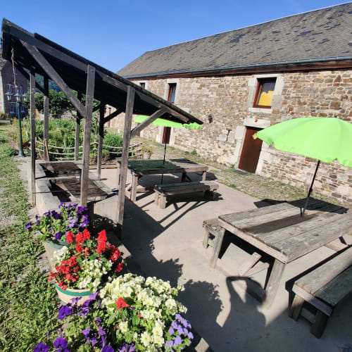 Terrasse extérieure de La Ferme De Werpin avec tables de pique-nique en bois, parasols et fleurs colorées à Hotton, Belgique