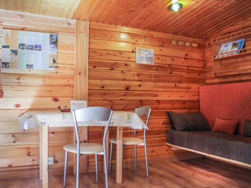Interior acogedor de cabaña de madera con mesa de comedor, sillas y sofá rojo en Turismo en Sanabria, Zamora