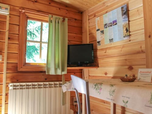 Acogedora habitación de cabaña de madera en Turismo en Sanabria con ventana, calefacción, televisor y carteles informativos en las paredes