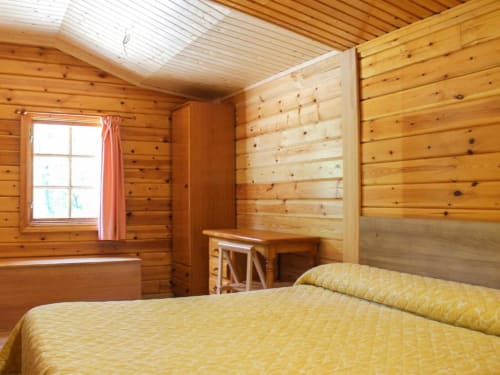 Dormitorio de cabaña de madera con ropa de cama amarilla en Turismo en Sanabria, Zamora. Acogedora habitación con paredes de pino y ventana.