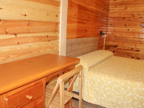 Acogedora habitación de cabaña de madera en Turismo en Sanabria con paredes rústicas de troncos, cama con ropa de cama color crema y mesita de noche de madera