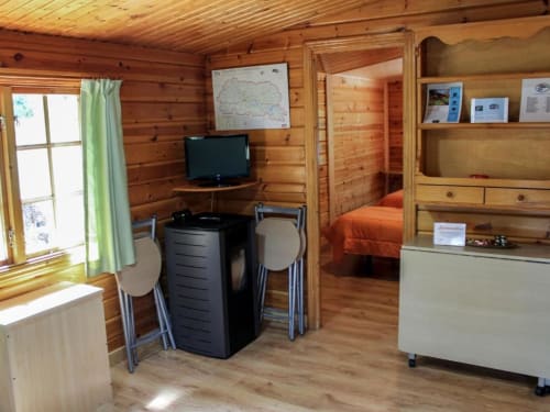Interior de cabaña de madera con sala de estar, TV, escritorio con sillas y dormitorio en Turismo en Sanabria, Vigo Zamora
