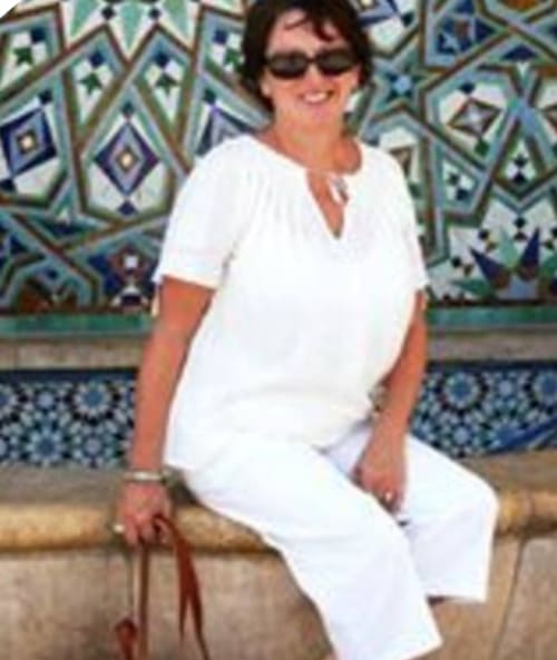 Femme en tenue blanche souriante à la Maison d'hôtes Chez Anne Marie à Beausemblant, France, avec un mur de carrelage décoratifen arrière-plan