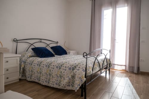 Camera luminosa a La Casetta di Pietra B&B a Gavorrano con letto in ferro battuto, biancheria floreale e porte a vetri verso la terrazza