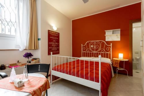 Camera rossa presso Alloggio Le Casette a Verona con letto in metallo bianco, biancheria rossa, scrivania e comfort moderni