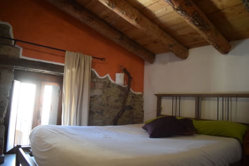 Habitación rústica en el hostal La Calma De Bellver con vigas de madera vistas, pared naranja y vistas al valle desde el balcón
