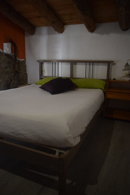 Acogedora habitación en el hostal La Calma De Bellver con cama blanca, almohadas verde lima, estructura de madera y vigas vistas en Bellver de
