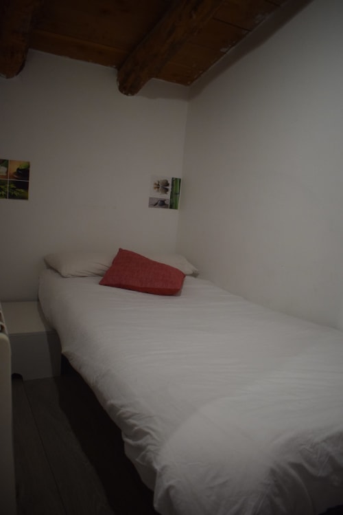 Habitación sencilla en el hostal La Calma De Bellver con cama blanca, almohada roja y vigas de madera vistas