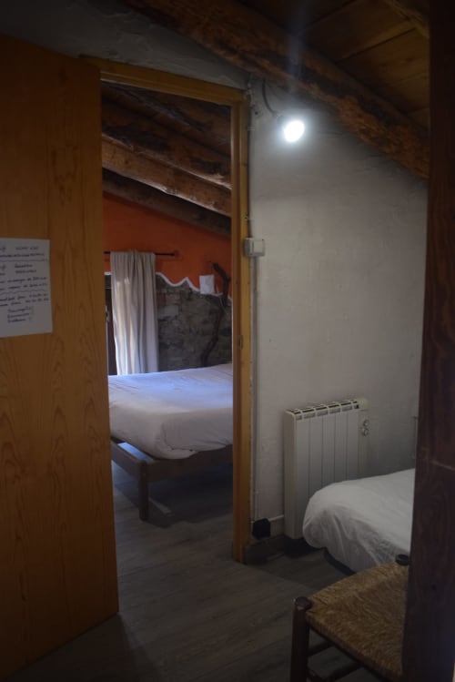 Habitación de albergue en La Calma De Bellver con cama, radiador y puerta hacia el dormitorio adyacente en Bellver de la Cerdanya
