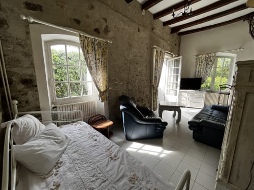 Chambre spacieuse à Aux Fleurs de Cerises avec lit blanc, salon noir, poutres apparentes et vue sur jardin