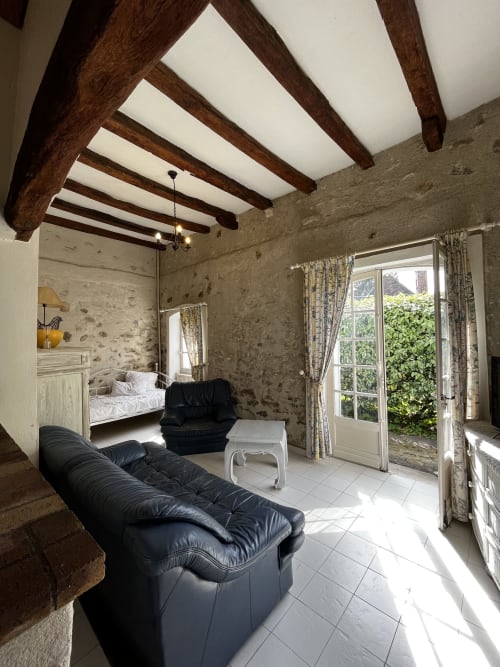 Chambre spacieuse avec poutres apparentes, sièges en cuir noir, murs en pierre et portes sur jardin aux Fleurs