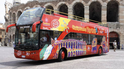 Red double-decker hop-on hop-off tour bus in Verona with historic Roman amphitheater backdrop