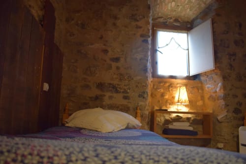 Dormitorio rústico en el hostal La Calma De Bellver en Bellver de la Cerdanya con muros de piedra, cama, lámpara y vistas a las montañas