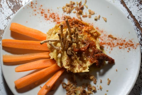 Plato gourmet presentado en el albergue La Calma De Bellver con hummus, cebolla caramelizada, bastones de zanahoria y pimentón.