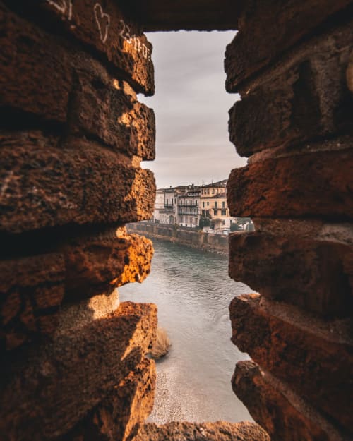 Historic brick archway framing Verona waterfront with colorful buildings along the river