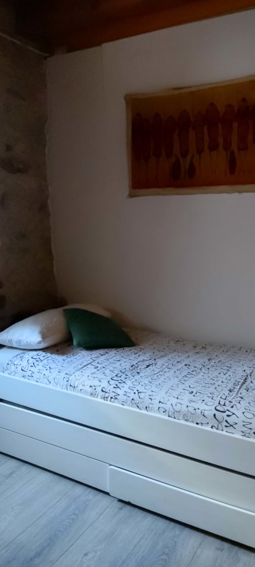 Habitación sencilla de hostal en La Calma De Bellver con cama blanca, almohada verde y póster de vistas a la montaña en la pared
