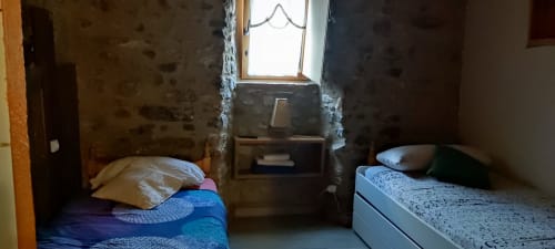Dormitorio de albergue en La Calma De Bellver con dos camas, paredes de piedra, ventana con vista a la montaña y servicios básicos en Bellver