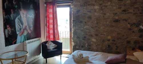 Acogedora habitación del hostel La Calma De Bellver con cama, silla negra, balcón con vistas a la montaña y paredes de piedra