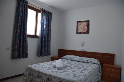 Acogedora habitación en la Pensión Eva de Puerto de Mogán con cama de madera, cortinas azules estampadas y decoración mural
